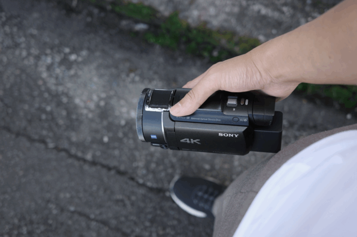 探偵が屋外で撮影準備を行う様子。浮気調査で使用するSONY製4Kビデオカメラを手に持っている。